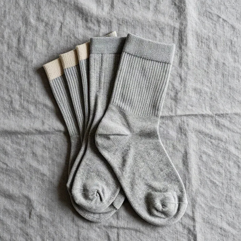 Three heather-grey crew socks fanned on ash-grey linen in a top-down studio flat lay.